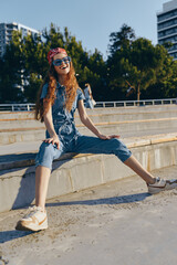 Lifestyle woman in modern boho-western denim street style sitting outdoors, smiling with sunglasses and headband, captured with warm film color tones.