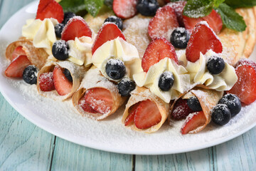 French crepes filled with whipped cream, strawberries, and blueberries, dusted with powdered sugar.