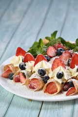 French crepes filled with whipped cream, strawberries, and blueberries, dusted with powdered sugar