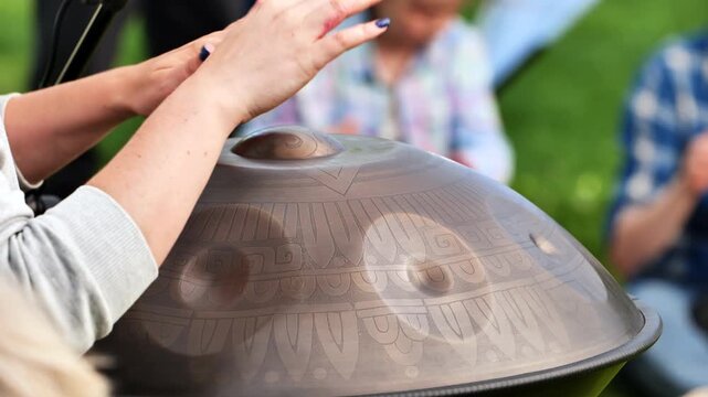 Musician playing handpan percussion instrument, creating soothing sounds outdoors