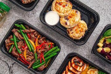 Nutritious meal prep containers with beef stir fry, pancakes, grilled chicken, and salad on gray background