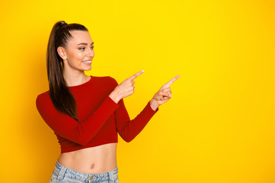 Fototapeta Young woman in red cropped top smiles and points to the right against a bright yellow background for lifestyle fashion and shopping advertising