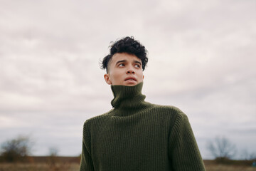 A candid portrait of a young man in a dark green turtleneck sweater, conveying authenticity and...