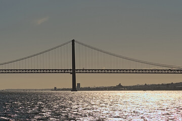 Silhouette of Ponte 25 de Abril bridge over Tagus river against a colorful evening sky, with sunlight reflecting in the water Lisbon, Portugal 