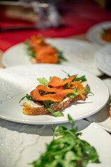 Fresh bruschetta with smoked salmon, arugula, and cream cheese served on sesame bread slice on white plate