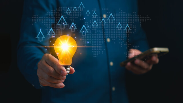 Innovation and business growth concept showing person holding glowing light bulb with rising arrows and digital world map, symbolizing creativity, success, and global development.