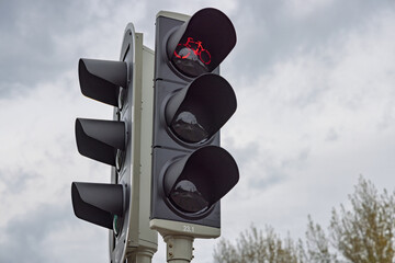 Close-up of a modern traffic light for bicycles, showing the red stop signal with the distinctive illuminated bicycle symbol against a cloudy sky.