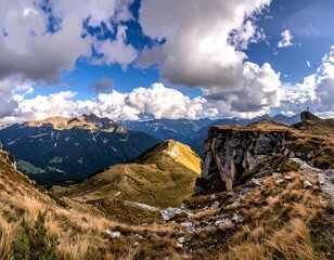 A sweeping vista showcases rugged mountains and valleys under a dramatic sky. Sunlight highlights peaks and cliffs with a lone figure