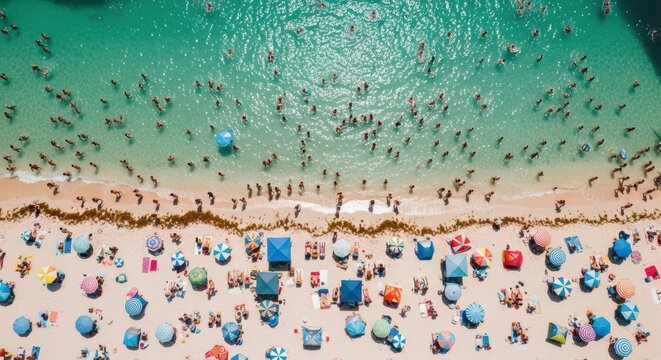 Aerial drone view of a crowded beach scene. People swimming in turquoise water and relaxing on sand. Colorful umbrellas creating a vibrant pattern. Summer vacation and holiday travel concept