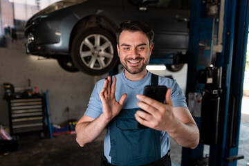 Mechanic smiles while talking on smartphone in busy garage during the day