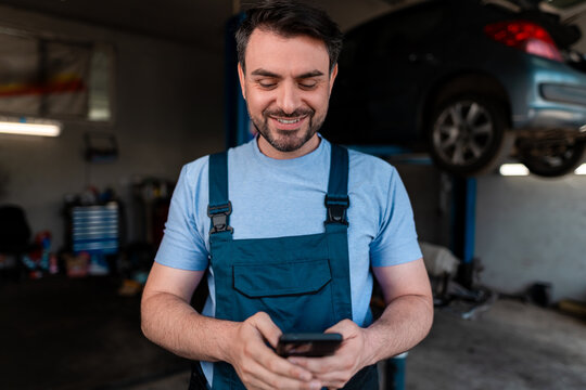 Mechanic checks phone while working in an auto repair shop during the day - Powered by Adobe
