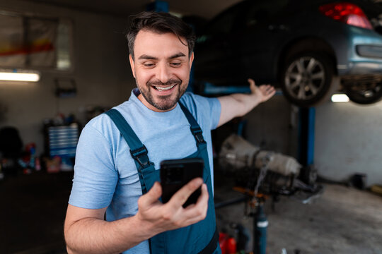 Happy mechanic checking phone while working in auto repair shop