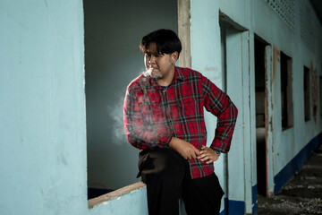 A young man sits alone and smokes a cigarette in an abandoned building.