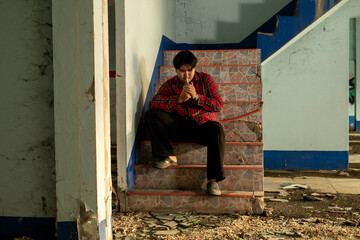 Young Asian man in a plaid shirt sitting and smokes a cigarette in abandoned building alone.