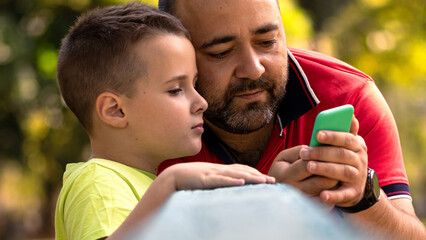 A boy and a man looking at a mobile phone screen. Father and son using a smartphone