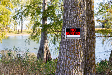 No hunting sign posted on a tree by lake. Hunting season, trespassing and hunting laws concept.