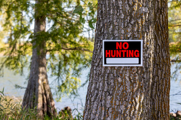 No hunting sign posted on a tree by lake. Hunting season, trespassing and hunting laws concept.