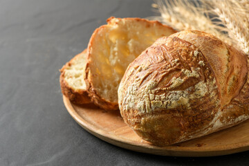 crusty artisanal sourdough loaf, presented on a rustic wooden plate with a bunch of golden wheat