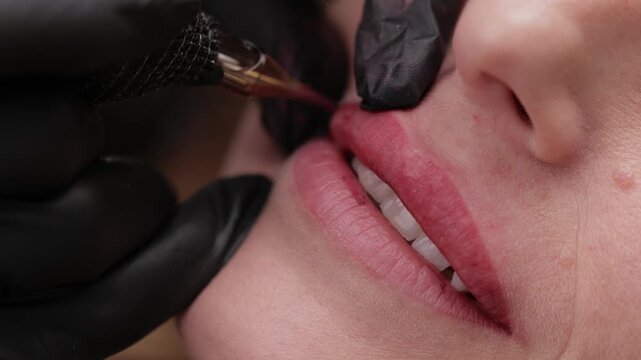 Tattoo procedure on young female lips by gloved technician.