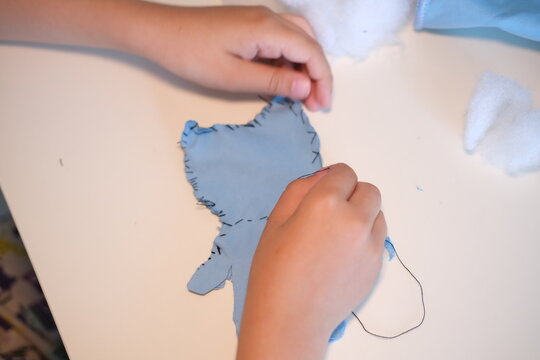 Top view. Children's hands hold a needle and thread and learn to sew.