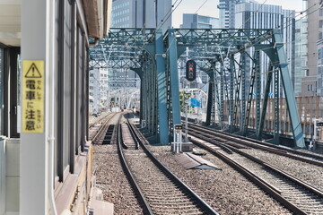 都会の駅のホームに停車するマルーン色の電車と鉄道の線路｜高層ビルを背景にした日本の都市風景