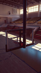Sunlight fills the empty gymnasium highlighting a lone basketball hoop. Rows of seats wait for spectators as shadows dance across the wooden floor in the quiet space.