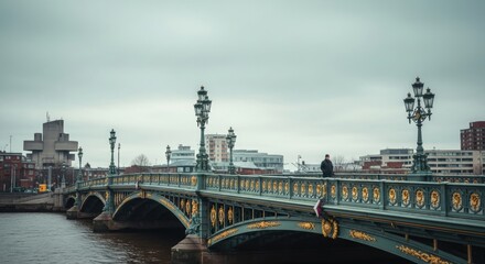 Fototapeta premium Ornate historic bridge over a city river. Solitary adult male walking across the urban crossing. Cinematic cityscape with a moody atmosphere. Concept of journey and urban exploration