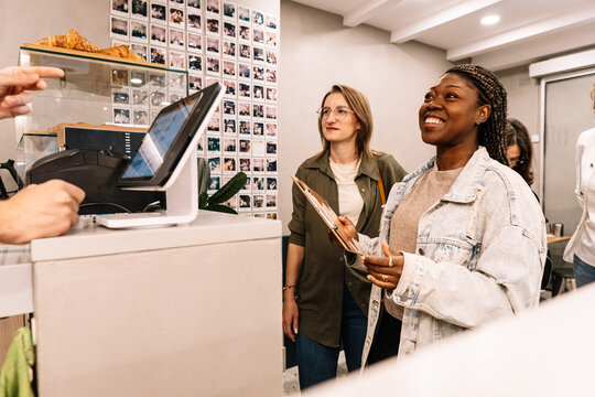 Multiethnic women ordering from a cafe counter smiling