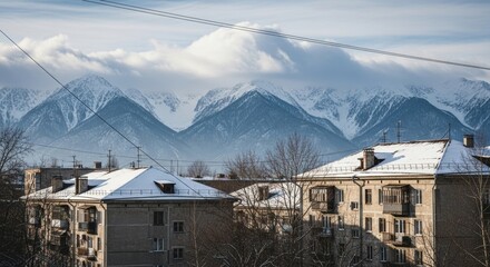 Old residential buildings in a provincial town. Snow covered rooftops in winter. Majestic mountain range landscape. Post soviet architecture and remote living concept