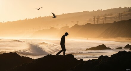 Solitary male silhouette walking on a rocky shore during a golden sunset. Contemplative scene with ocean waves. Concept for mental health awareness and personal journey. Overcoming adversity