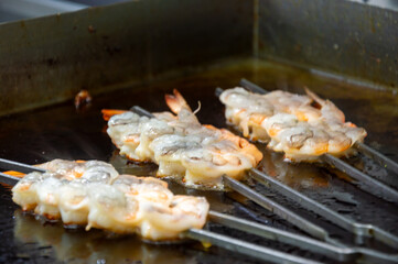 Shrimp skewers sizzle on a hot grill as chefs prepare for a vibrant culinary event in a lively kitchen