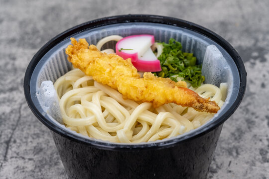Bowl of Asian Udon noodles with broth and a tempura shrimp and egg on top for a hearty meal.