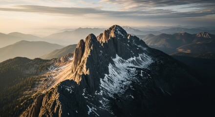 Rugged mountain peak with snow at sunset. Cinematic aerial view of an alpine landscape. Adventure travel and exploration concept. Metaphor for challenge success and reaching the summit