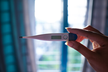 Hand holding digital thermometer indoors with soft natural light. Health and temperature...