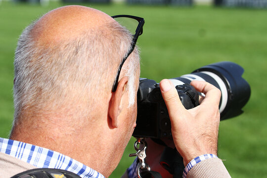 Fototapeta Fotógrafo senior profesional calvo fotografiando y enfocando con cámara con teleobjetivo y hierba de fondo