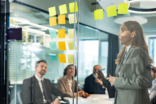 Businesspeople talking in their diverse team during a brainstorming session with sticky notes on glass wall in a modern office