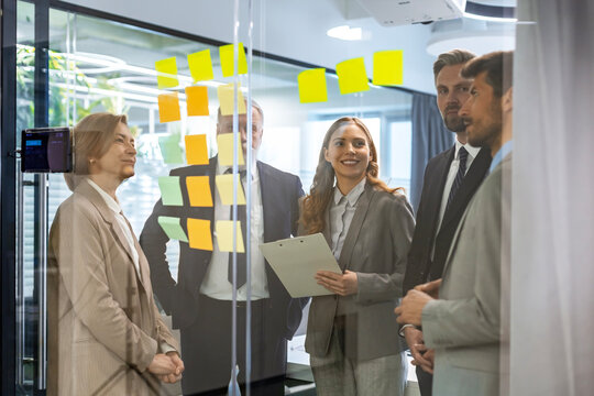 Businesspeople talking in their diverse team during a brainstorming session with sticky notes on glass wall in a modern office
