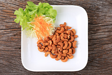 Roasted cashew nuts arranged on a white plate, garnished with shredded cabbage and carrots