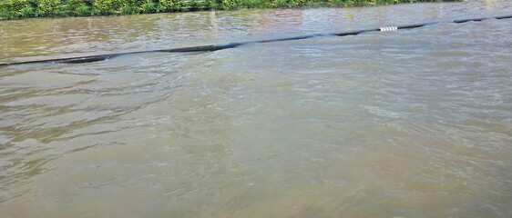 The curb is flooded. The river water has overflowed the road so that the edge of the road cannot be seen. Water has waves caused by the force of passing cars. Cars cannot drive through. Dangerous 
