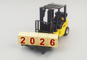 Yellow forklift truck carrying wooden cubes with numbers 2026 on grey background. Symbol of new year 2026.