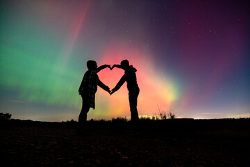 Couple hands forming heart during aurora borealis display