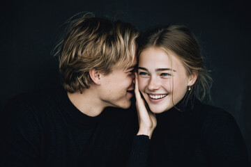 A couple sharing a joyful moment, one whispering a secret into the other's ear, sparking laughter and intimacy, captured in soft lighting with an emphasis on their expressive features and emotional co