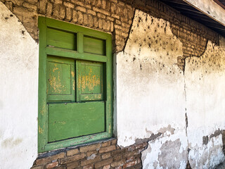 Closed old Javanese wooden window with green shutters on an broken white concrete wall. Concept for traditional exterior, vintage, heritage, rural housing ornament. Empty blank copy text space.
