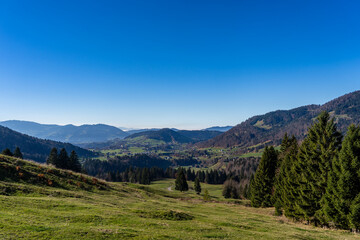 misty but serene view mountain valley with green fields and distant hills under clear blue sky in Bregenzer Wald in Vorarlberg Austria