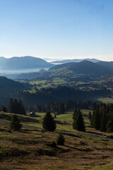 misty but serene view mountain valley with green fields and distant hills under clear blue sky in Bregenzer Wald in Vorarlberg Austria