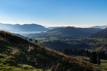 misty but serene view mountain valley with green fields and distant hills under clear blue sky in Bregenzer Wald in Vorarlberg Austria