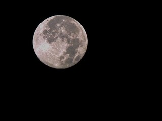 Bright full moon shines in a clear night sky illuminating the darkness with its glowing light and intricate surface details