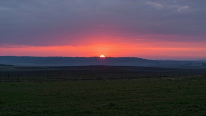 Vibrant sunset paints the sky with fiery colors over rolling hills and serene countryside landscape