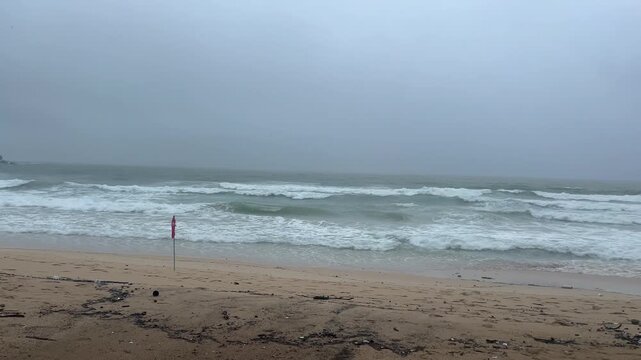 Stormy ocean with large waves crashing on a sandy beach. A red warning flag indicates dangerous swimming conditions during a hurricane