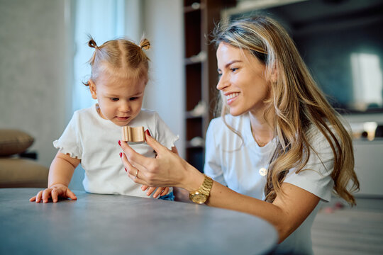 Happy mother and curious toddler daughter bonding while exploring a wooden toy block, fostering learning and child development